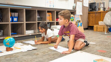 two students working on the floor with paper and pencil