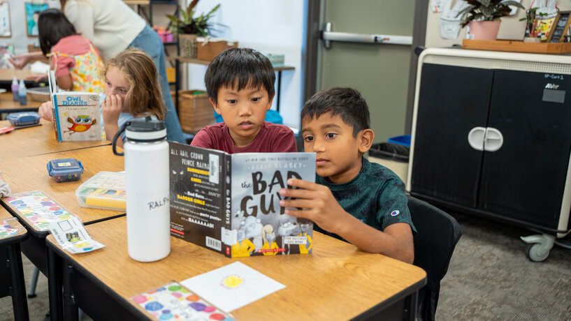 twp boys sitting at a desk and reading a book together