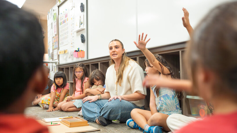 teacher sitting on a floor surrounded by students